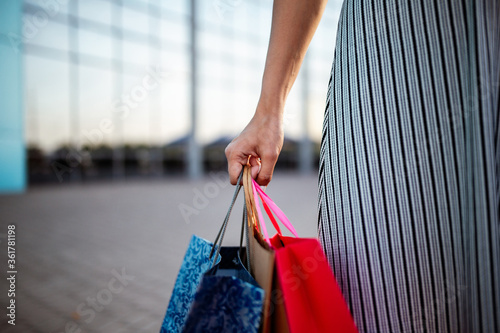 Closeup of young attractive woman holding a few shopping bags with newly purchased goods and clothes. Girl holds colourful packs full of bought things in her hands. Shopping and spendings concept.