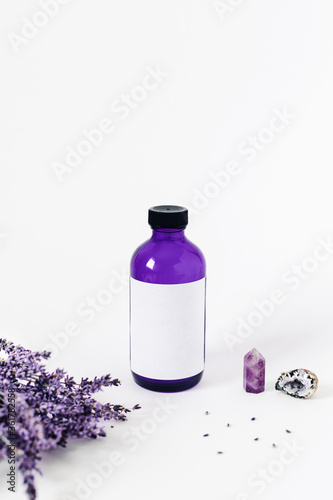 Purple glass bottle on white background surrounded by lavender bouquet and the crystal of quartz. Energy of stones for your home.