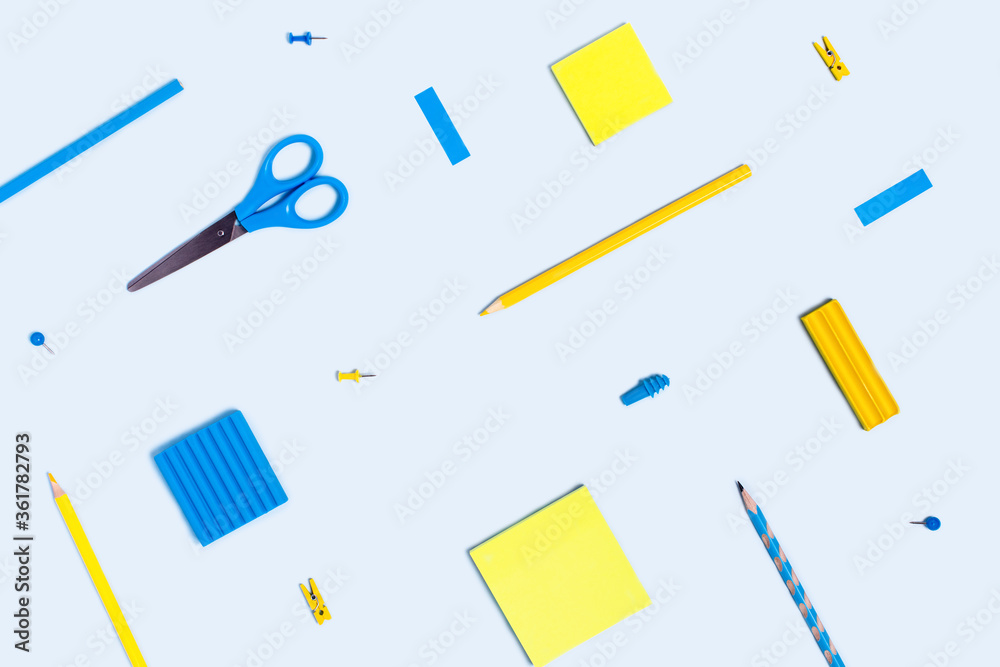 Blue background with writing materials. Back to school flat lay with blue and yellow pencils, paper clips, scissors and notepads on blue background. Blue background with writing materials. Back to school flat lay with blue and yellow pencils, paper clips, scissors and notepads on blue background.
