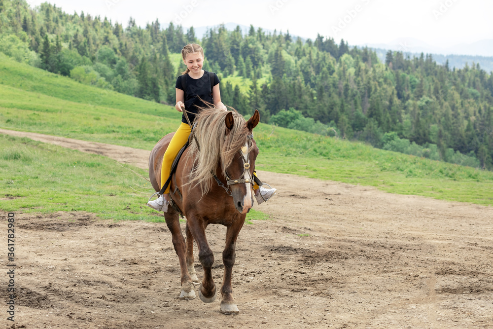 Happy teenager girl riding a horse on a mountainous area. The girl spends her leisure time with a smile. She likes this hobby. Happy teenager girl riding a horse on a mountainous area. The girl spends her leisure time with a smile. She likes this hobby.