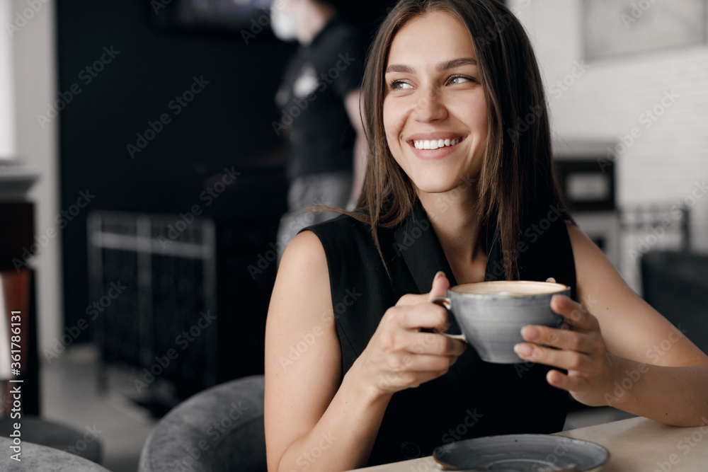 Portrait of a young smiling woman in cafe with coffee cup and phone