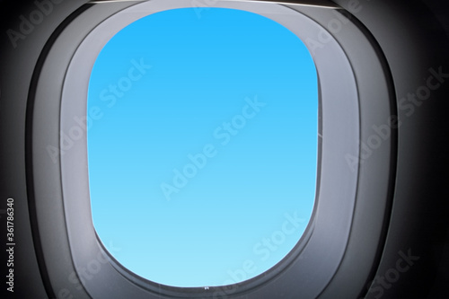 airplane window interior against blue sky background. Side closeup view of passenger aircraft window frame. Modern plane cabin interior. Design template with copy space for aviation theme