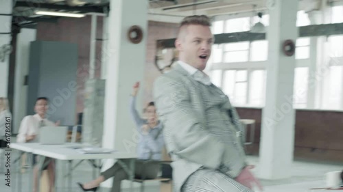 The young manager expressively dances with a glass in the office and throws it. Colleagues having fun break in working hours. Jokes in the office.