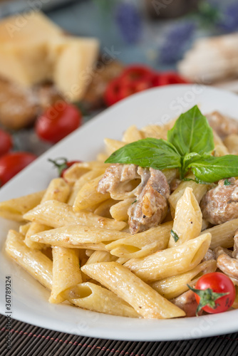 Penne pasta in creamy sauce with chicken, tomatoes decorated with parsley