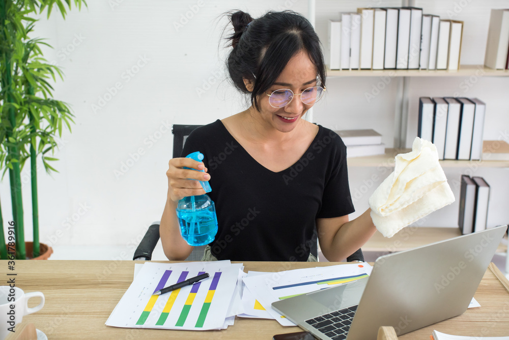 Young woman cleaning the surface of laptop with alcohol spray and fabric at home Young woman cleaning the surface of laptop with alcohol spray and fabric at home