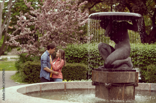 Young, happy, loving couple having date in the park near fountain. Relations, friendship and love.