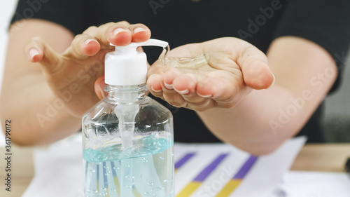 Business woman cleaning hands with sanitizer alcohol gel while working on her desk.