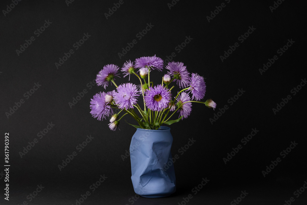 a bright bouquet of purple daisies on a black background. simple spring and summer story, contrasting still life, decoration for the interior of the kitchen or bedroom.