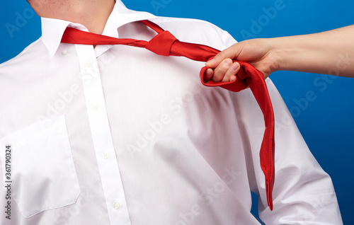 female hand pulls a red silk tie around the neck of an adult man dressed in a white shirt, concept of violence at work