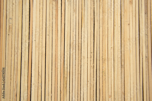 Thin wooden slats of light wood lie close to each other vertically. View from above. Background and textures