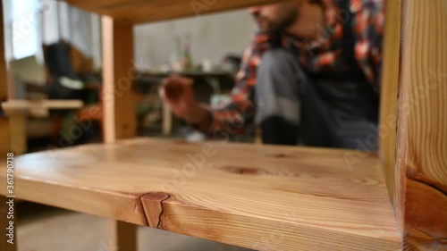 Woodworker puts varnish on a wooden table.Worker is painting wooden details in factory of producing furniture. Hand of man with brush is applying drying oil