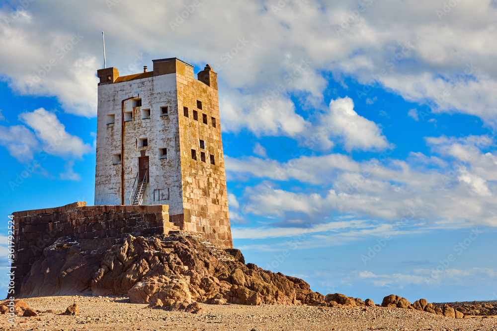 Image of Seymour Tower at low tide with stones, cloudy sky and sunshine.
