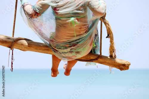 Woman swinging on a wooden swing against the blue sea. Beach holidays on a tropical resort, concept of freedom, happiness and romance