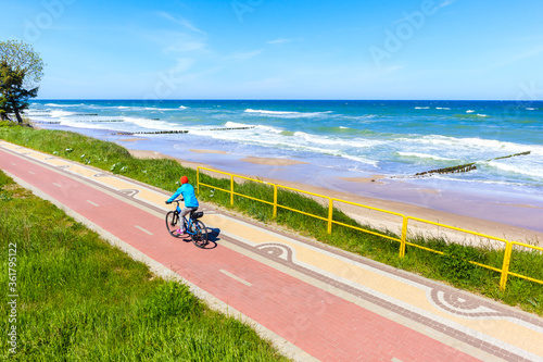 Quadro su tela Young woman cyclist riding bike along beautiful beach with near Kolobrzeg town,