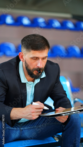 A young coach with beard in blazer sitting with tablet on bench