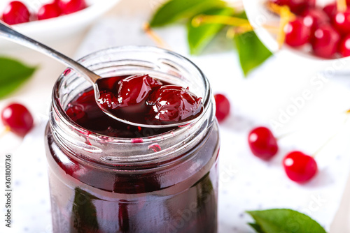 Close-up cherry jam in a glass jar. Homemade sweet cherry jam and fresh cherry on a white table