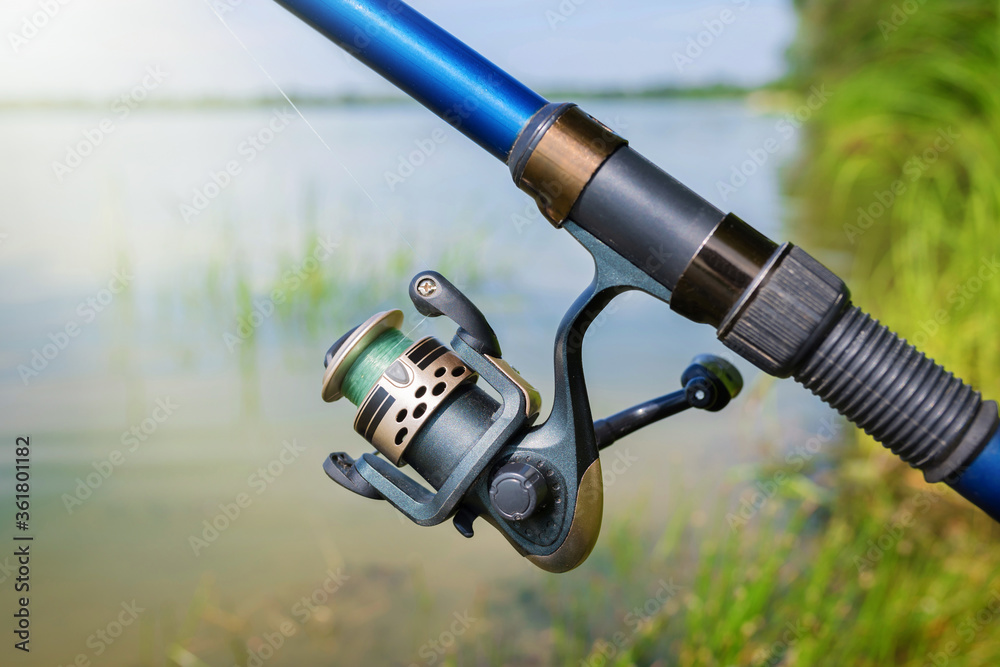Fishing rod with reel on the background of the lake on a sunny day. Fishing background. Leisure. Fishing rod with reel on the background of the lake on a sunny day. Fishing background. Leisure.