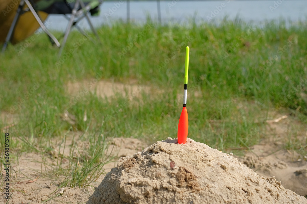 Fototapeta premium Fishing float in the sand on the lake. Fishing background.