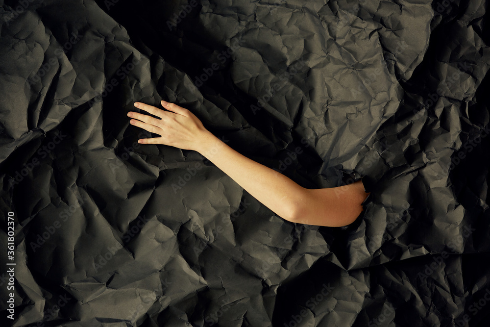 Woman's hand comes out of hole in black crumpled paper background, a concept photography for beauty blog Woman's hand comes out of hole in black crumpled paper background, a concept photography for beauty blog