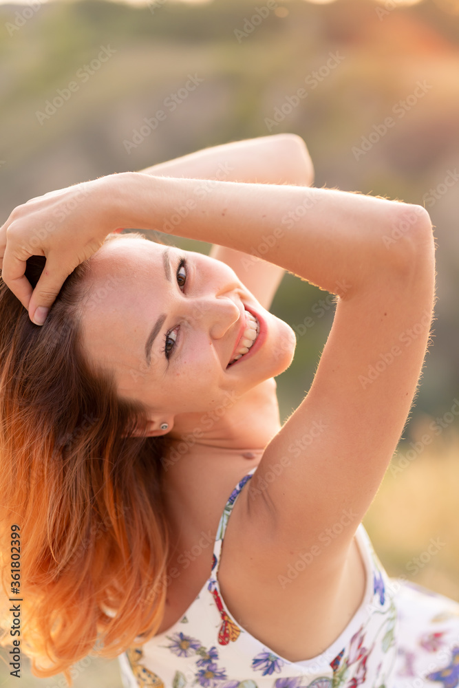 Tender beautiful red-haired girl enjoys the sunset in a field with a hill.