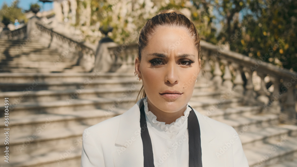 Young beautiful upset woman angrily looking in camera on stairs in old park. Sad face expression Young beautiful upset woman angrily looking in camera on stairs in old park. Sad face expression