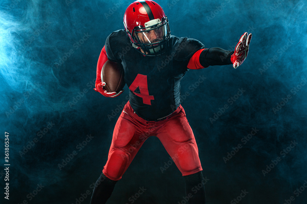 American football player, athlete sportsman in red helmet on dark background with smoke. Sport and motivation wallpaper.