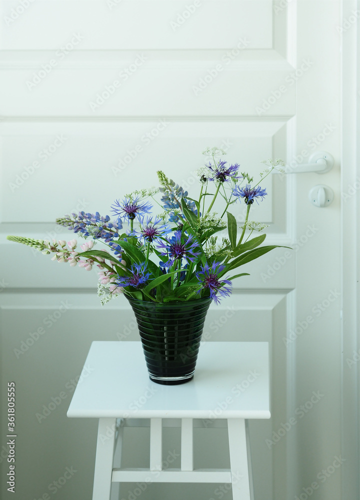 Close-up wildflower bouquet in glass vase on the white table. White background. Wild flowers at home. Cornflowers in vase. Close-up wildflower bouquet in glass vase on the white table. White background. Wild flowers at home. Cornflowers in vase.