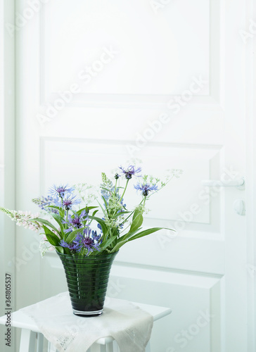 Close-up wildflower bouquet in glass vase on the white table. White background. Wild flowers at home. Cornflowers in vase.