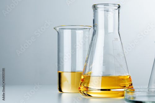 Laboratory glassware with yellow oily liquid on grey background