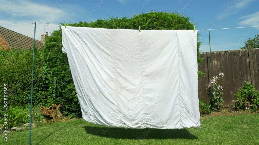 A wet double bed quilt, hanging out to dry on a washing line in a garden / yard,  blowing in the breeze in the summer sunshine.