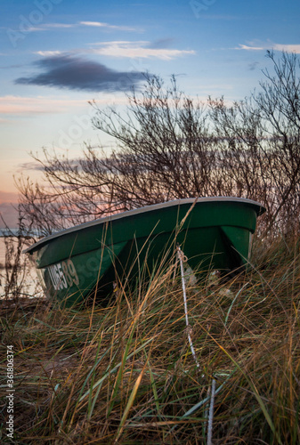 Green boat anchored on a grass-covered sand dune during sunset, Latvia.