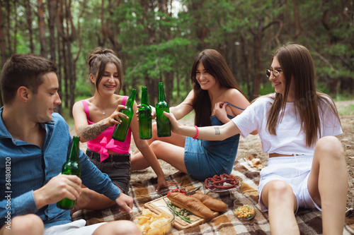 Happiness. Group of friends clinking beer bottles during picnic in summer forest. Lifestyle  friendship  having fun  weekend and resting concept. Looks cheerful  happy  celebrating  festive.