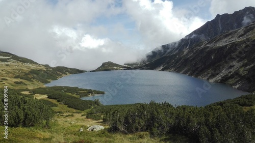 Close up clear lake inside mountain glen, opening on blue sky and calm clouds, seen from a hiker perspective