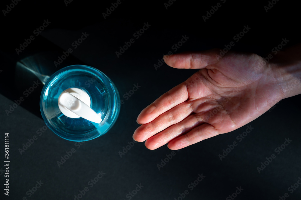 Top view of woman hand waiting alcohol sanitizer in pump bottle for cleaning hand on black background, dark tone