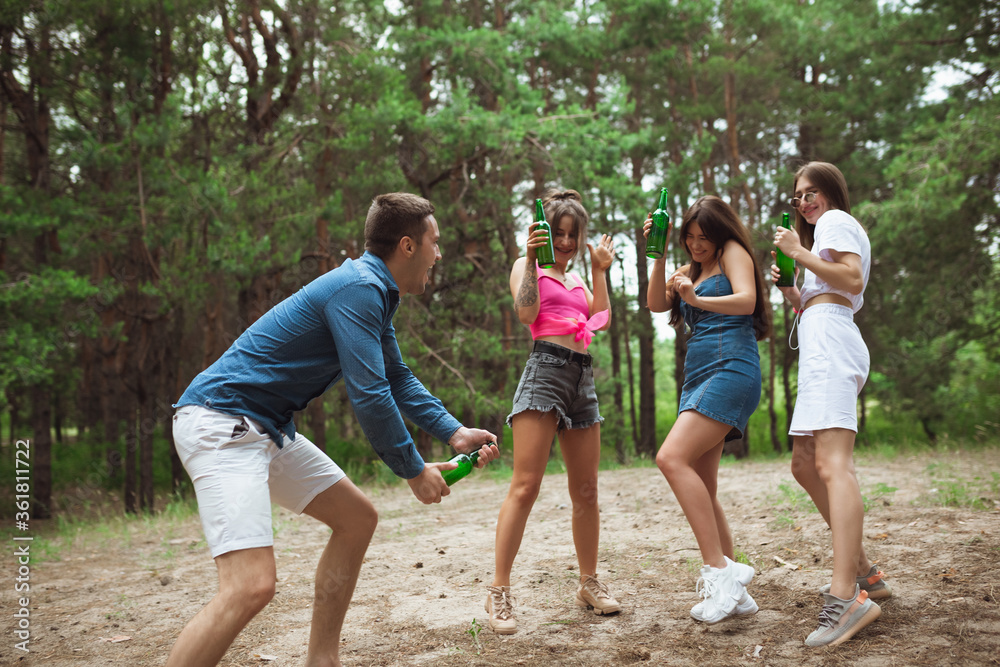 Fototapeta premium On the way. Group of friends walking down together during picnic in summer forest. Lifestyle, friendship, having fun, weekend and resting concept. Looks cheerful, happy, celebrating, festive.
