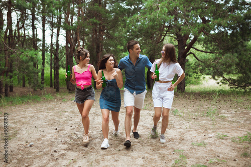 On the way. Group of friends walking down together during picnic in summer forest. Lifestyle, friendship, having fun, weekend and resting concept. Looks cheerful, happy, celebrating, festive.