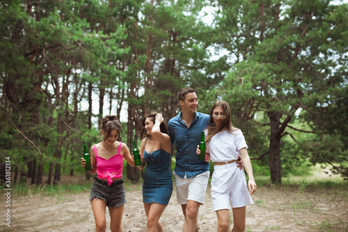 On the way. Group of friends walking down together during picnic in summer forest. Lifestyle, friendship, having fun, weekend and resting concept. Looks cheerful, happy, celebrating, festive.