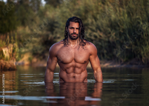 Leinwand Poster Long haired bearded muscular man shirtless stands waist deep in the water