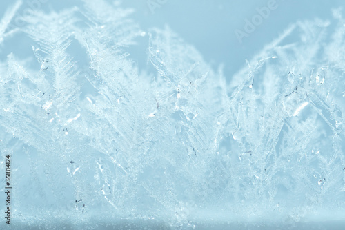 Closeup winter window pane coated shiny icy frosted patterns. Abstract beautiful ice flowers pattern, macro view background. Snowflakes on winter glass, natural texture. New year Christmas backdrop.
