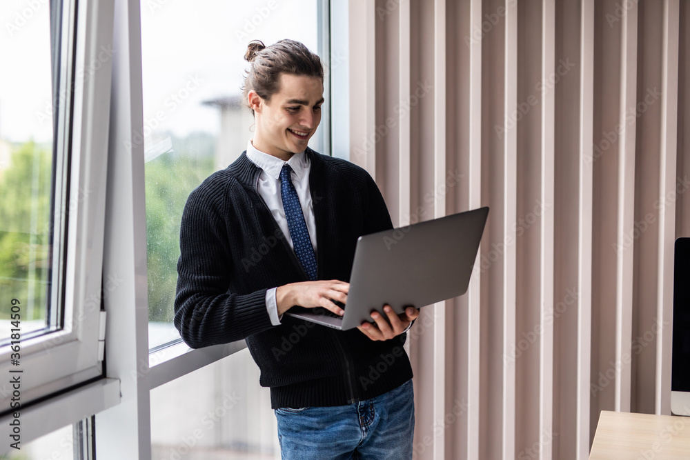 Portrait of handsome businessman smiling while using laptop in office Portrait of handsome businessman smiling while using laptop in office