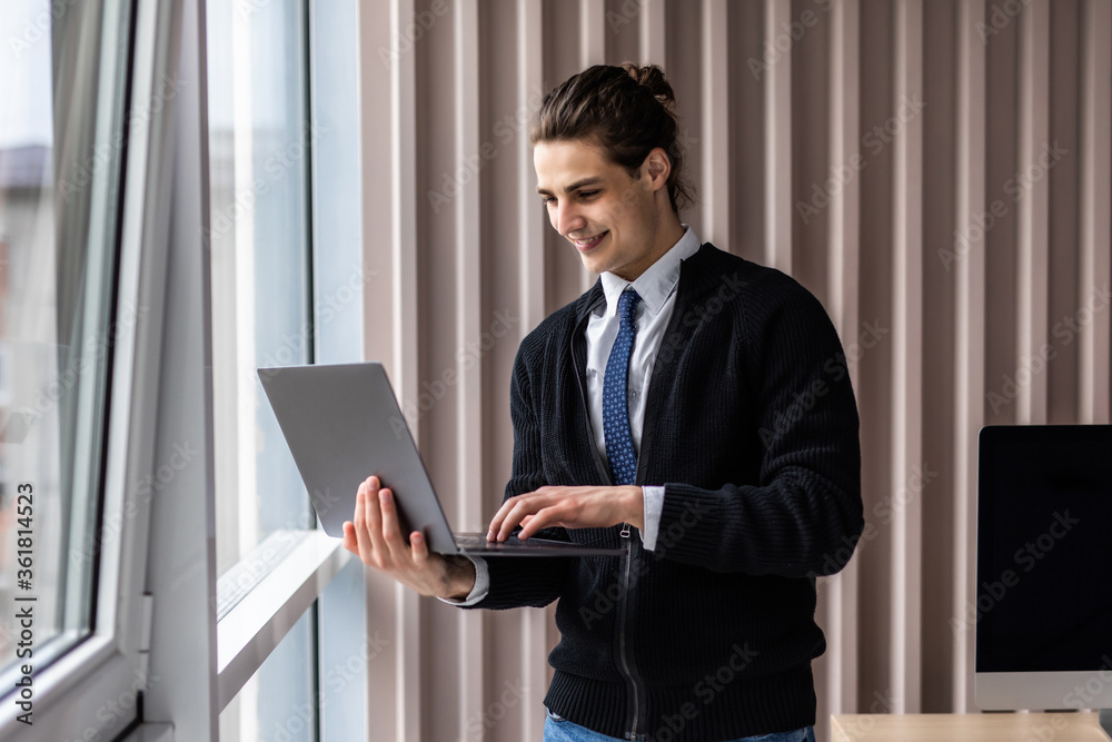 Portrait of handsome businessman smiling while using laptop in office Portrait of handsome businessman smiling while using laptop in office