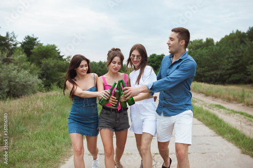 On the way. Group of friends clinking beer bottles during picnic in summer forest. Lifestyle, friendship, having fun, weekend and resting concept. Looks cheerful, happy, celebrating, festive.