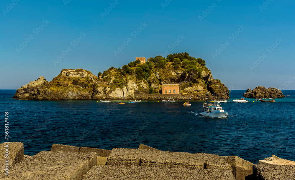 The Isole dei Ciclopi island and stacks offshore viewed from the harbour wall at Aci Trezza, Sicily in summer