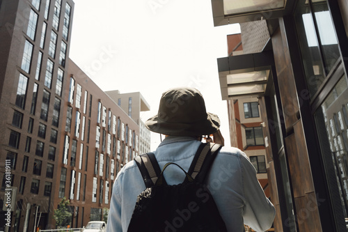 Tourist man travels around city. A guy with a backpack and a hat, a traveler is walking around the city and talking on the phone. Hipster with a beard. Communication technology in an urban environment