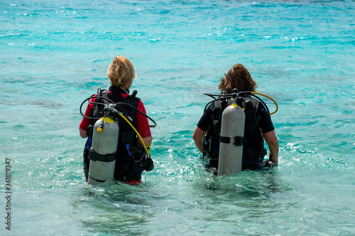 Two caucasian women with diving cylinders on their backs walking in the Caribbean Ocean of Bonaire going to dive