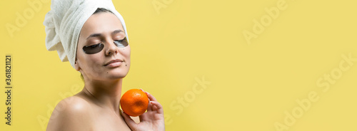 Beauty portrait of woman in white towel on head with gold nourishing mask on face. Skincare cleansing eco organic cosmetic spa relax concept. A girl stands with her back holding an orange mandarin.