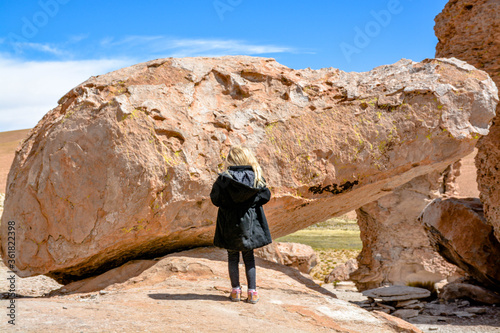 Little girl facing a big rock in the Laguna Colorada in Bolivia