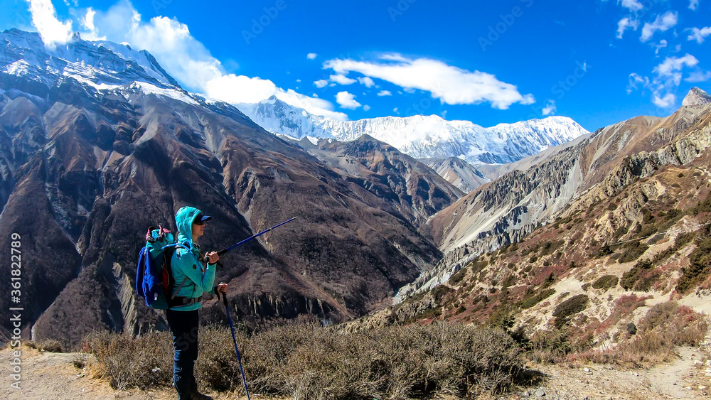 A woman pointing with a hiking stick to the peaks in front, while exploring Annapurna Circus in Himalayas, Nepal. Dry and desolated landscape. High, snow capped mountain peaks. Happiness and freedom
