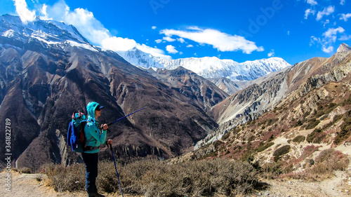 A woman pointing with a hiking stick to the peaks in front, while exploring Annapurna Circus in Himalayas, Nepal. Dry and desolated landscape. High, snow capped mountain peaks. Happiness and freedom