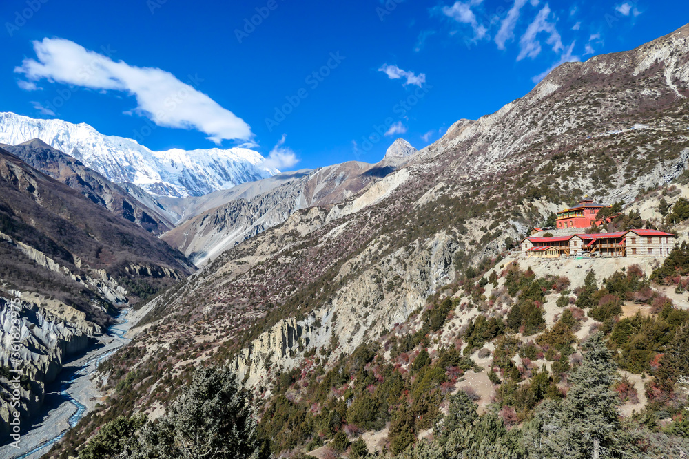 A temple complex in a valley along Annapurna Circuit in Nepal. IN the back there are high, snow capped Himalayan peaks. Slopes are overgrown with small bushes. Spirituality and meditation